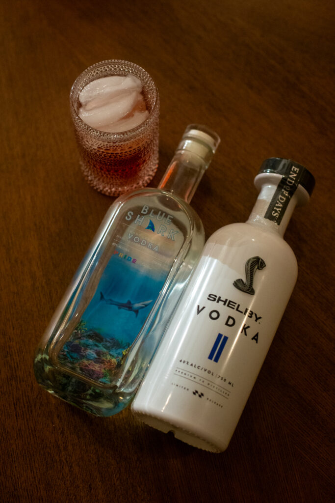 Two vodka bottles laying on a table with a poured cocktail