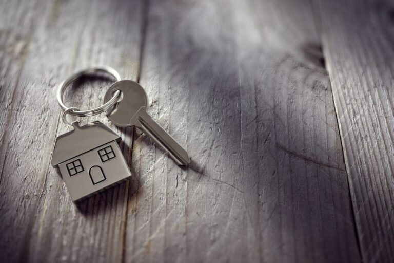 House key on a house-shaped keychain resting on wooden floorboards