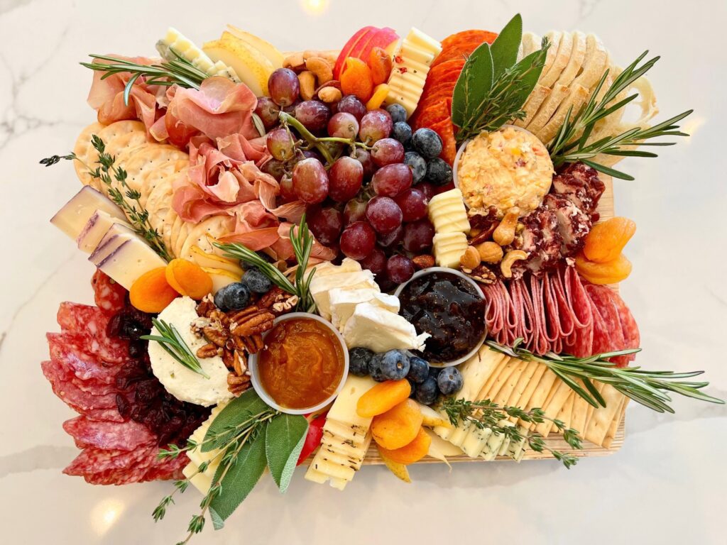 Overhead shot of Boundless Boards charcuterie board, a business that grew from just a side hustle over the pandemic. Grapes, jams, herbs, nuts, cheeses, and meats.