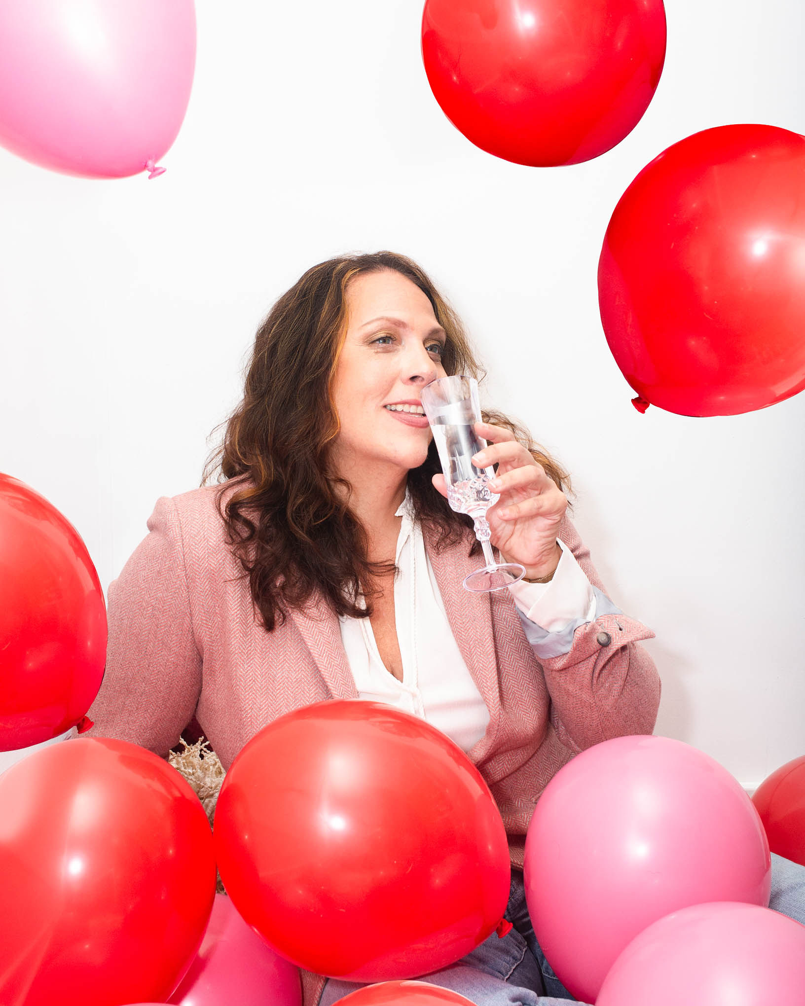 Andrea Arth drinking champagne and surrounded by pink and red balloons, date night spots recommendations for Wilmington, NC