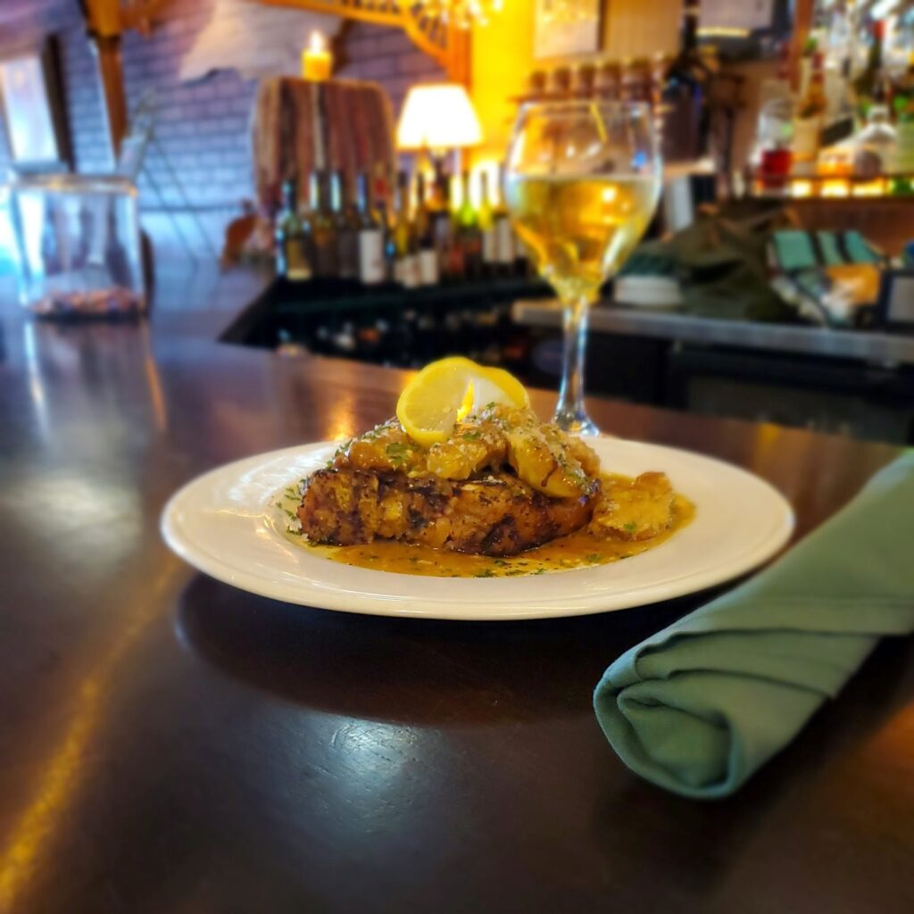 Italian dish with glass of white wine and silverware wrapped in a green cloth napkin, at the bar Freddie's Restaurant of Kure Beach date night spot