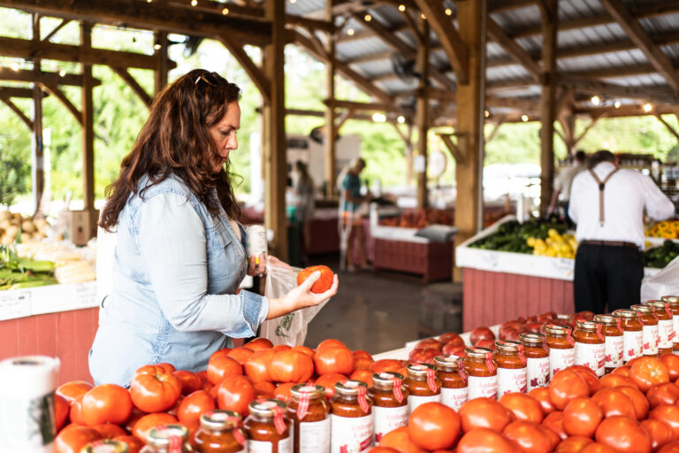 Andrea Arth picking up a tomato from a farmers market stand.