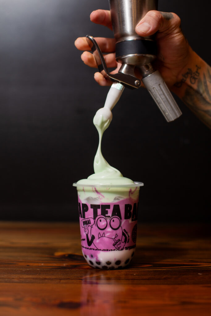 Pink boba tea with whipped topping being added from TAP Tea Bar for Local Spots for College Students on a Budget Arth Real Estate Group