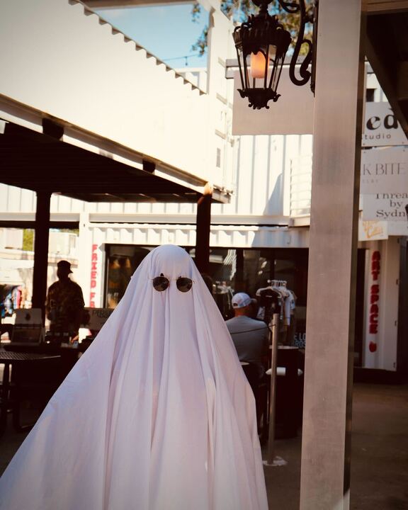 Person in a sheet and sunglasses posing like a ghost outside Bookworm Pottery in the Cargo District